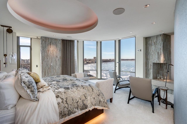 carpeted bedroom with a tray ceiling, floor to ceiling windows, and a water view