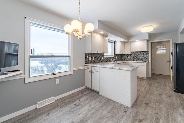 kitchen featuring refrigerator, hanging light fixtures, tasteful backsplash, a wealth of natural light, and white cabinets