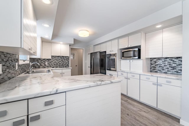 kitchen with stainless steel appliances, white cabinetry, sink, and light stone counters