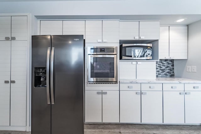 kitchen with appliances with stainless steel finishes, light stone countertops, light hardwood / wood-style floors, white cabinets, and decorative backsplash