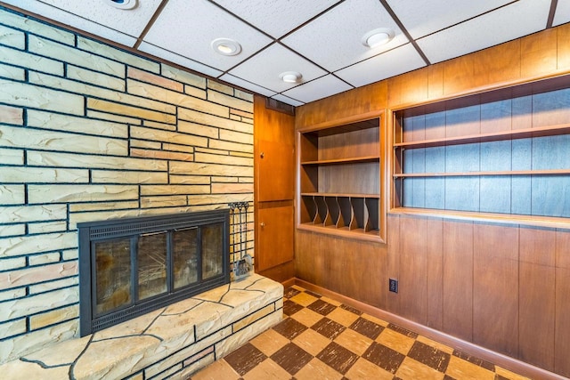 unfurnished living room featuring wood walls, a stone fireplace, built in features, and a drop ceiling