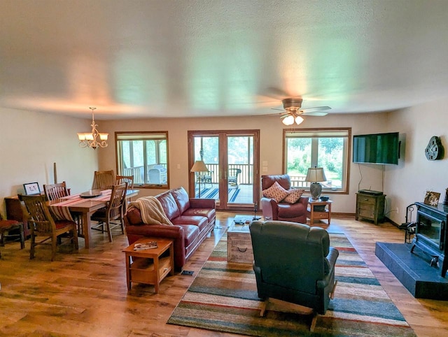 living room with ceiling fan with notable chandelier, wood-type flooring, and a wood stove