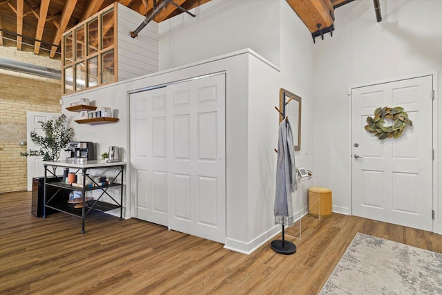 entryway with high vaulted ceiling, wooden ceiling, hardwood / wood-style flooring, brick wall, and beam ceiling