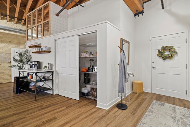 foyer entrance featuring beam ceiling, wood-type flooring, high vaulted ceiling, and brick wall