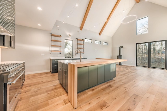 kitchen featuring high vaulted ceiling, high end stove, sink, a kitchen island with sink, and beam ceiling