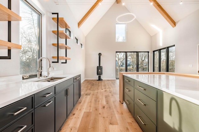 kitchen with sink, light hardwood / wood-style flooring, beam ceiling, high vaulted ceiling, and a wood stove