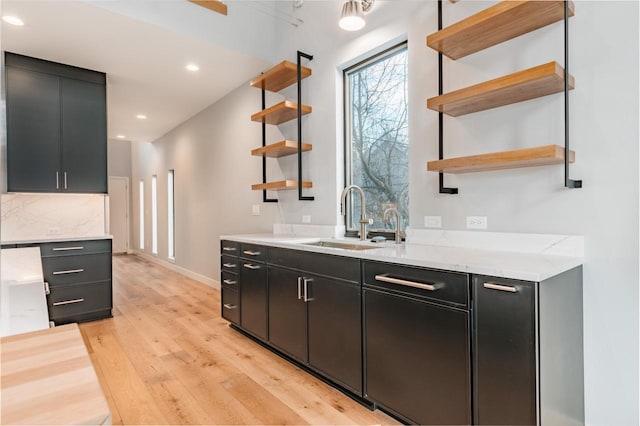 bar featuring tasteful backsplash, sink, light stone counters, and light hardwood / wood-style floors