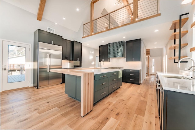 kitchen with high vaulted ceiling, beamed ceiling, stainless steel built in refrigerator, sink, and a center island with sink