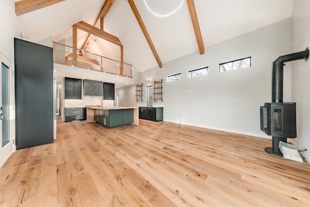 living room featuring beamed ceiling, high vaulted ceiling, light hardwood / wood-style flooring, and a wood stove