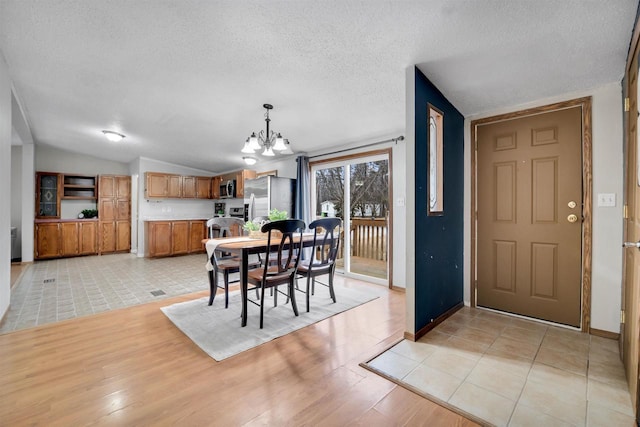 dining room featuring vaulted ceiling, light tile patterned floors, a notable chandelier, and a textured ceiling