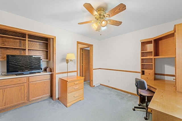 carpeted office space featuring wooden walls, built in desk, and ceiling fan