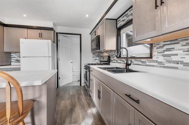 kitchen with dark hardwood / wood-style floors, stainless steel gas stove, sink, backsplash, and white refrigerator