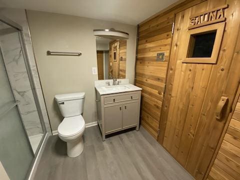 bathroom with toilet, vanity, wooden walls, a shower with door, and hardwood / wood-style floors