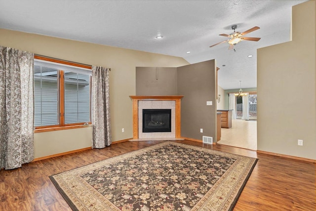 living room with a tile fireplace, vaulted ceiling, wood-type flooring, and ceiling fan with notable chandelier