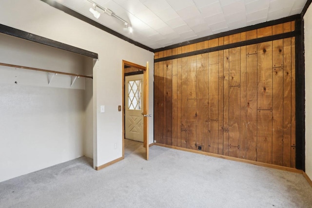 unfurnished bedroom featuring rail lighting, wooden walls, and light colored carpet