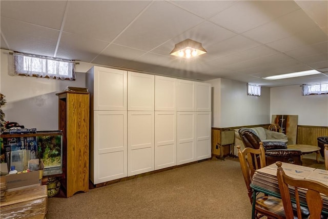 basement with a drop ceiling, wooden walls, and carpet flooring