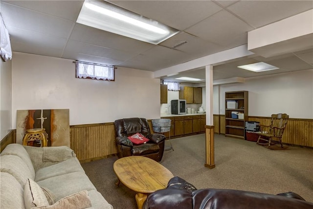 living room with a paneled ceiling, carpet floors, and wood walls