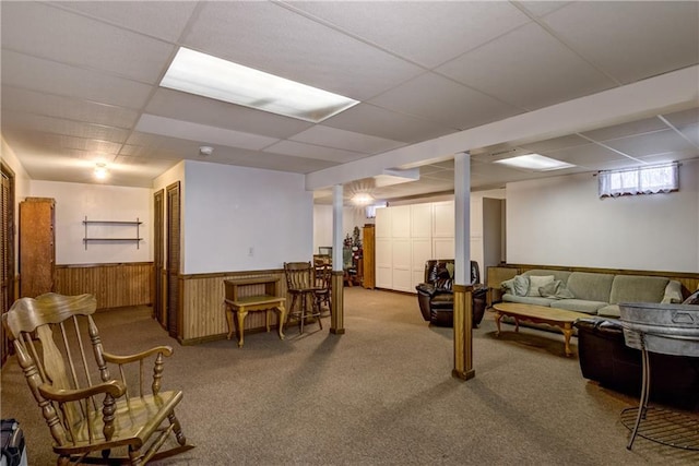 basement featuring a drop ceiling, carpet, and wood walls