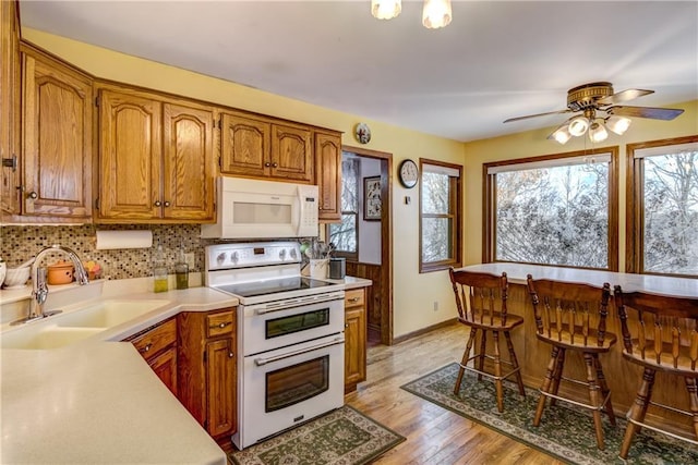 kitchen featuring sink, tasteful backsplash, light hardwood / wood-style flooring, ceiling fan, and white appliances