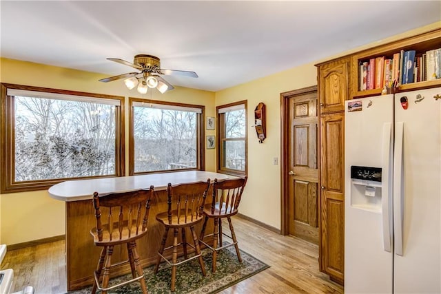 kitchen featuring a kitchen bar, white refrigerator with ice dispenser, a center island, and light wood-type flooring