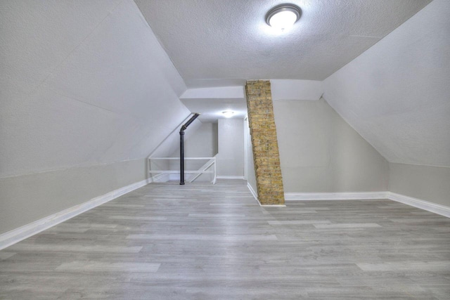 additional living space featuring hardwood / wood-style flooring, lofted ceiling, and a textured ceiling