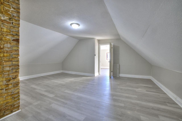 bonus room with vaulted ceiling, a textured ceiling, and light wood-type flooring