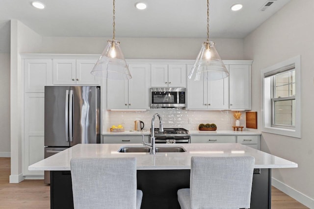 kitchen with a kitchen island with sink, a sink, white cabinetry, appliances with stainless steel finishes, and backsplash