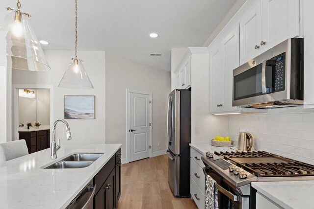 kitchen featuring light stone counters, pendant lighting, appliances with stainless steel finishes, white cabinetry, and a sink