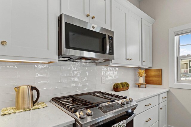 kitchen with stainless steel appliances, light stone counters, white cabinetry, and decorative backsplash