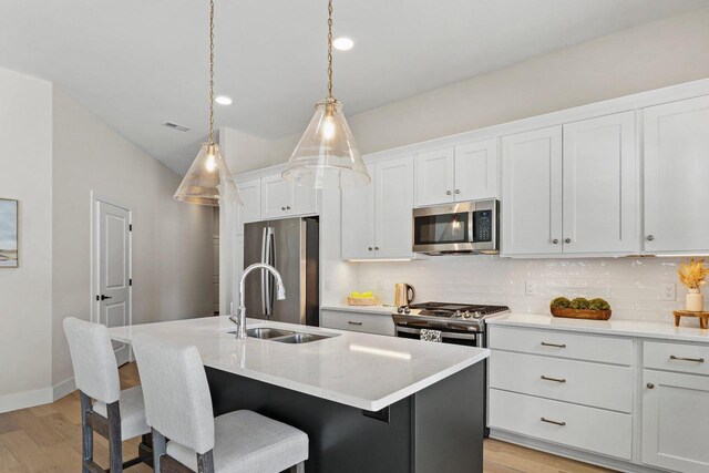 kitchen with a kitchen island with sink, stainless steel appliances, a sink, white cabinetry, and hanging light fixtures