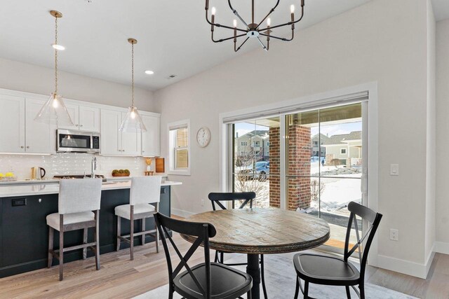 dining space with baseboards, light wood finished floors, and an inviting chandelier