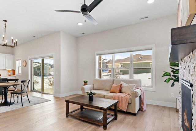 living area with a warm lit fireplace, visible vents, baseboards, and light wood finished floors