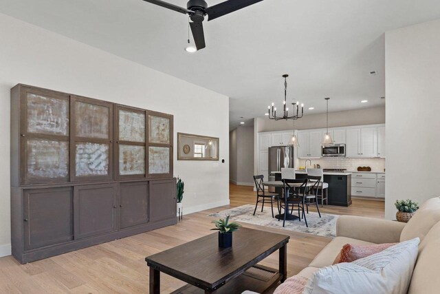 living area with light wood finished floors, baseboards, and ceiling fan with notable chandelier