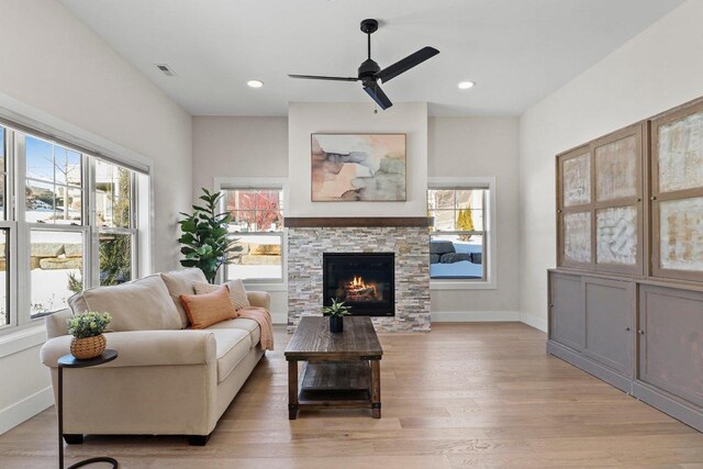 living area with a wealth of natural light, a stone fireplace, and light wood-style flooring