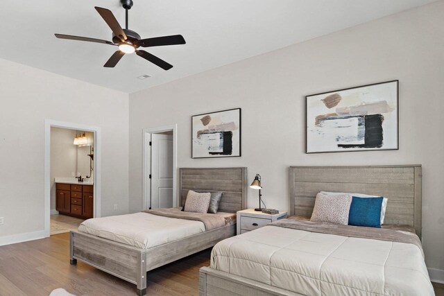 bedroom with a ceiling fan, ensuite bath, baseboards, and wood finished floors