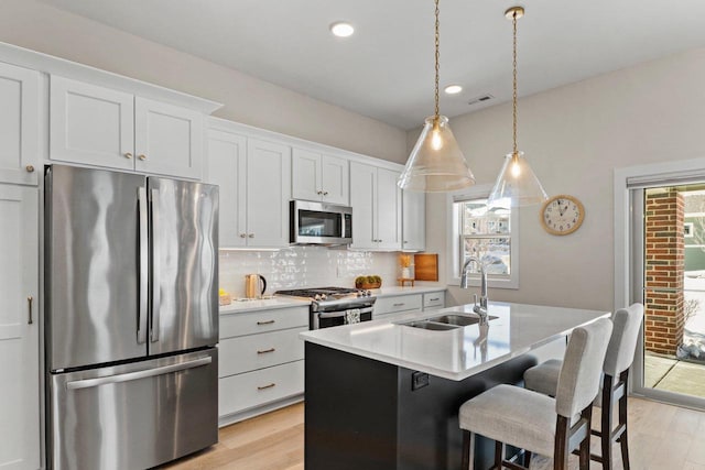 kitchen with pendant lighting, appliances with stainless steel finishes, white cabinetry, a sink, and an island with sink