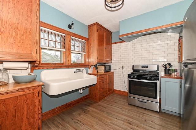 kitchen with sink, appliances with stainless steel finishes, backsplash, extractor fan, and dark hardwood / wood-style flooring