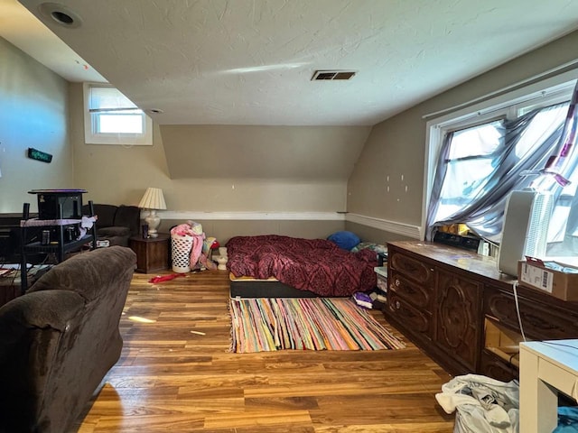 bedroom featuring lofted ceiling, a textured ceiling, and light hardwood / wood-style floors