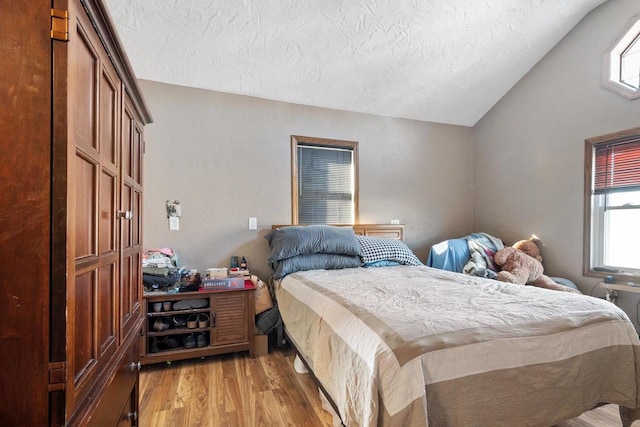 bedroom with lofted ceiling, a textured ceiling, and light wood-type flooring