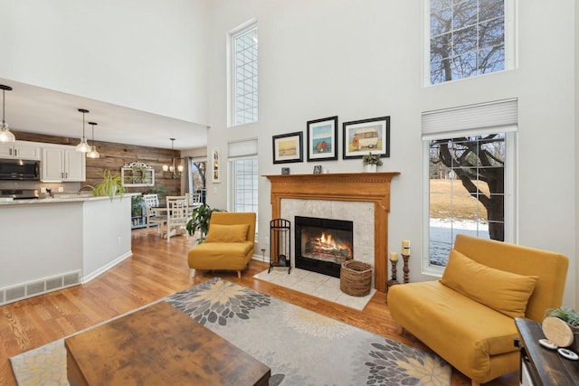 living room with an inviting chandelier, wooden walls, a towering ceiling, a high end fireplace, and light hardwood / wood-style floors