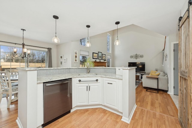 kitchen featuring decorative light fixtures, stainless steel dishwasher, white cabinets, a barn door, and backsplash