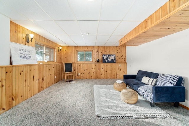 carpeted living room featuring a drop ceiling and wooden walls