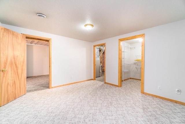 unfurnished bedroom with connected bathroom, a spacious closet, a textured ceiling, a closet, and light colored carpet