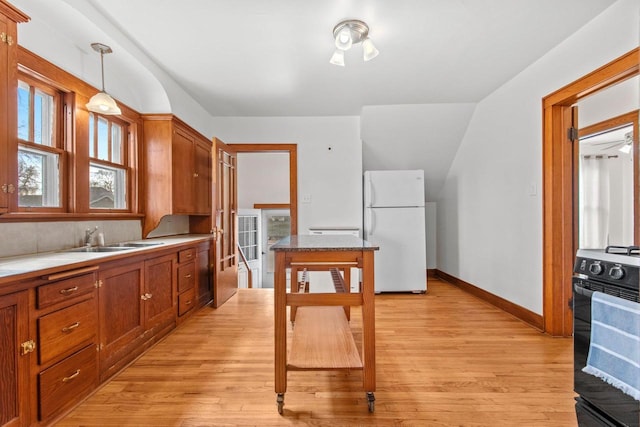 kitchen featuring sink, white refrigerator, hanging light fixtures, stove, and light hardwood / wood-style flooring