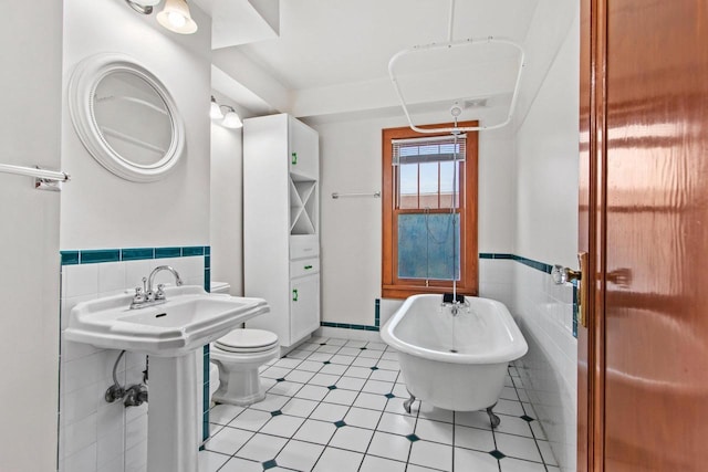 bathroom featuring tile patterned floors, toilet, tile walls, and a washtub