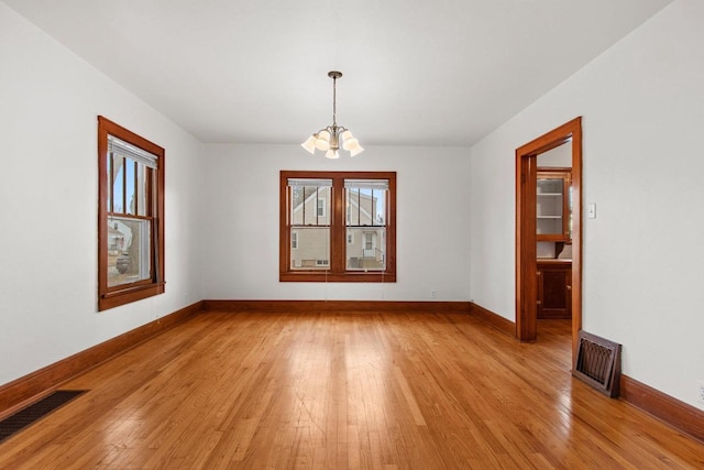 spare room with an inviting chandelier and light hardwood / wood-style floors