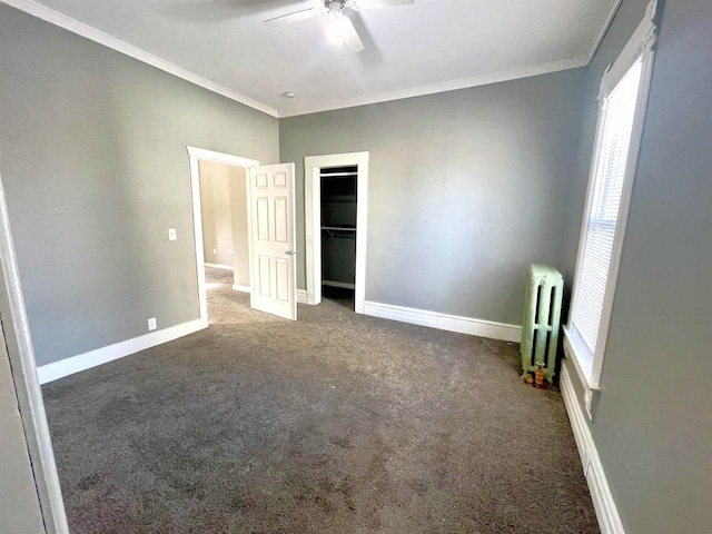 unfurnished bedroom with radiator heating unit, dark colored carpet, ceiling fan, crown molding, and a closet