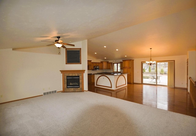 unfurnished living room featuring lofted ceiling, a fireplace, ceiling fan with notable chandelier, and light carpet