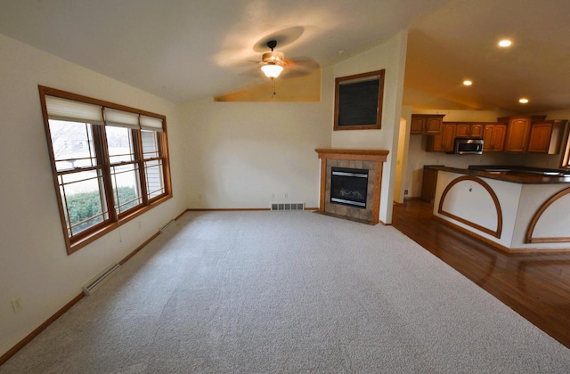 carpeted living room featuring a tiled fireplace, lofted ceiling, a baseboard heating unit, and ceiling fan