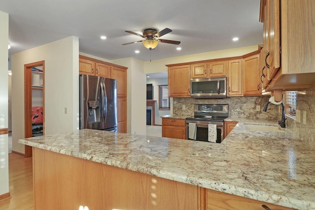 kitchen featuring appliances with stainless steel finishes, tasteful backsplash, sink, kitchen peninsula, and light stone countertops